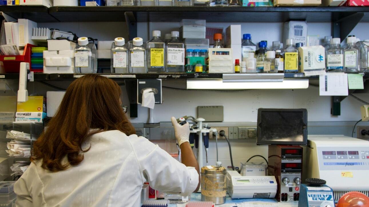 A laboratory technician in a white coat conducting STD testing in a research lab with various medical supplies and equipment on shelves.